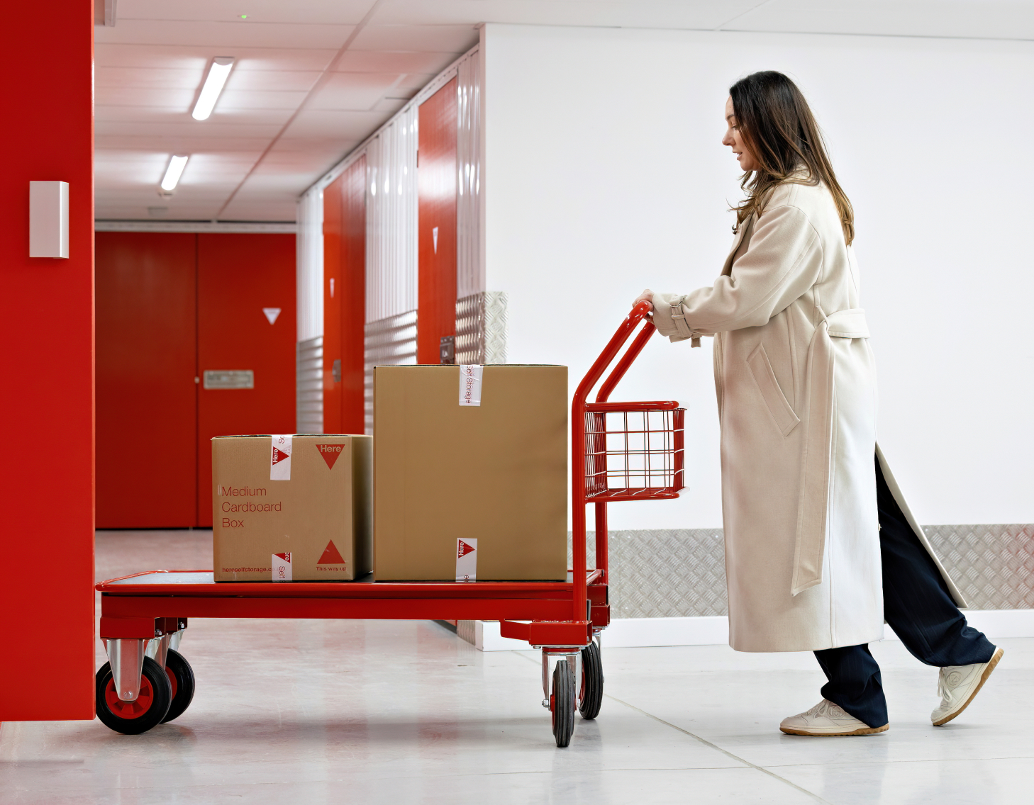 Woman with long coat pushes loading trolley with boxes into store lift