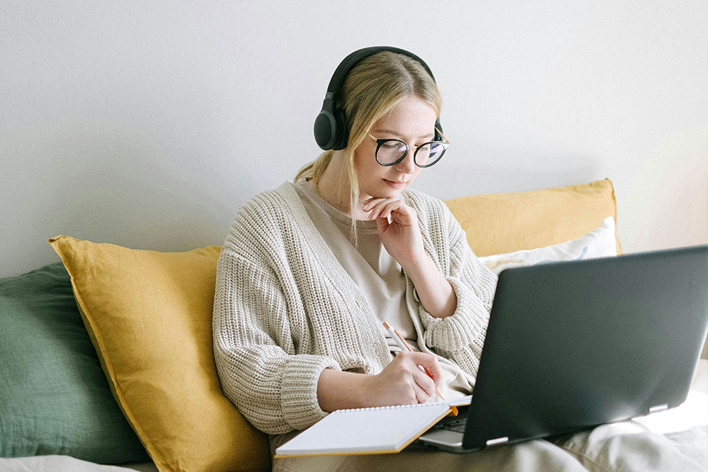 A young woman sat writing notes in front of her laptop whilst listening to music